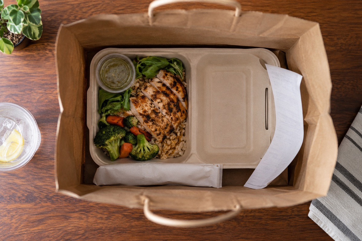 Opened takeout bag with one empty compartment, remaining neatly packed meal and receipt, overhead evidence-style composition.